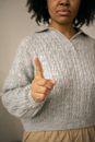 Crop unrecognizable African American female with dark curly hair in sweater pointing finger as restriction gesture against light wall