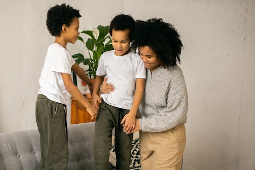 Cheerful black sons standing on couch near mother