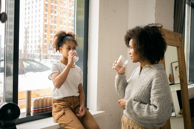 Black Mother With Daughter Drinking Water From Glasses