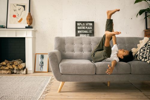Free Full body side view of joyful African American boy having fun while lying on sofa with raised legs in room Stock Photo