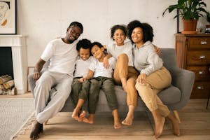 Full body of cheerful African American parents with children looking at camera while sitting on sofa in room with fireplace