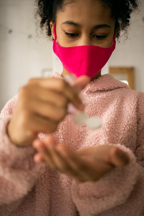 Black girl in protective mask applying antiseptic