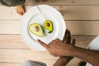 Top view of crop anonymous African American man pointing on organic healthy avocado helping child to choose between natural fruit and sweet lollipop