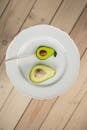 Top view half of ripe avocado with seed near lollipop in shape of avocado served on white plate against wooden floor