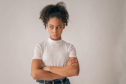 Concerned African American teenage girl in casual clothes looking away with displeased face while standing on white background in studio