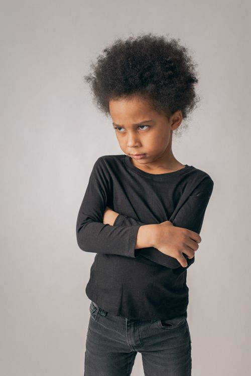 Free Offended African American girl with Afro hairstyle looking into distance while standing on white background with crossed arms in room Stock Photo