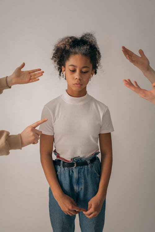 Crop people scolding disappointed African American teenage girl in casual wear standing on white background with sad face in studio
