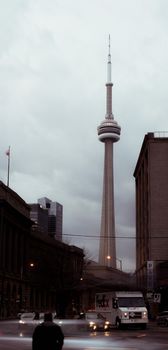 Famous CN tower located on street against overcast sky in city with residential buildings and roadway with automobiles in Toronto