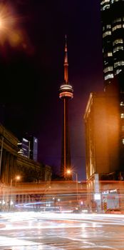 Modern CN tower located on dark street near road with glowing lights and modern buildings in city in night time