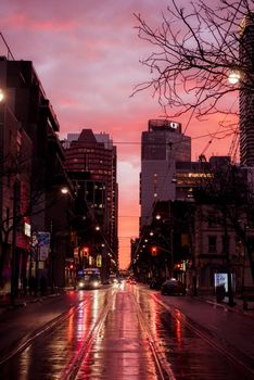 Straight wet roadway going between modern tall residential houses on street of modern city with glowing streetlamps at sunset time