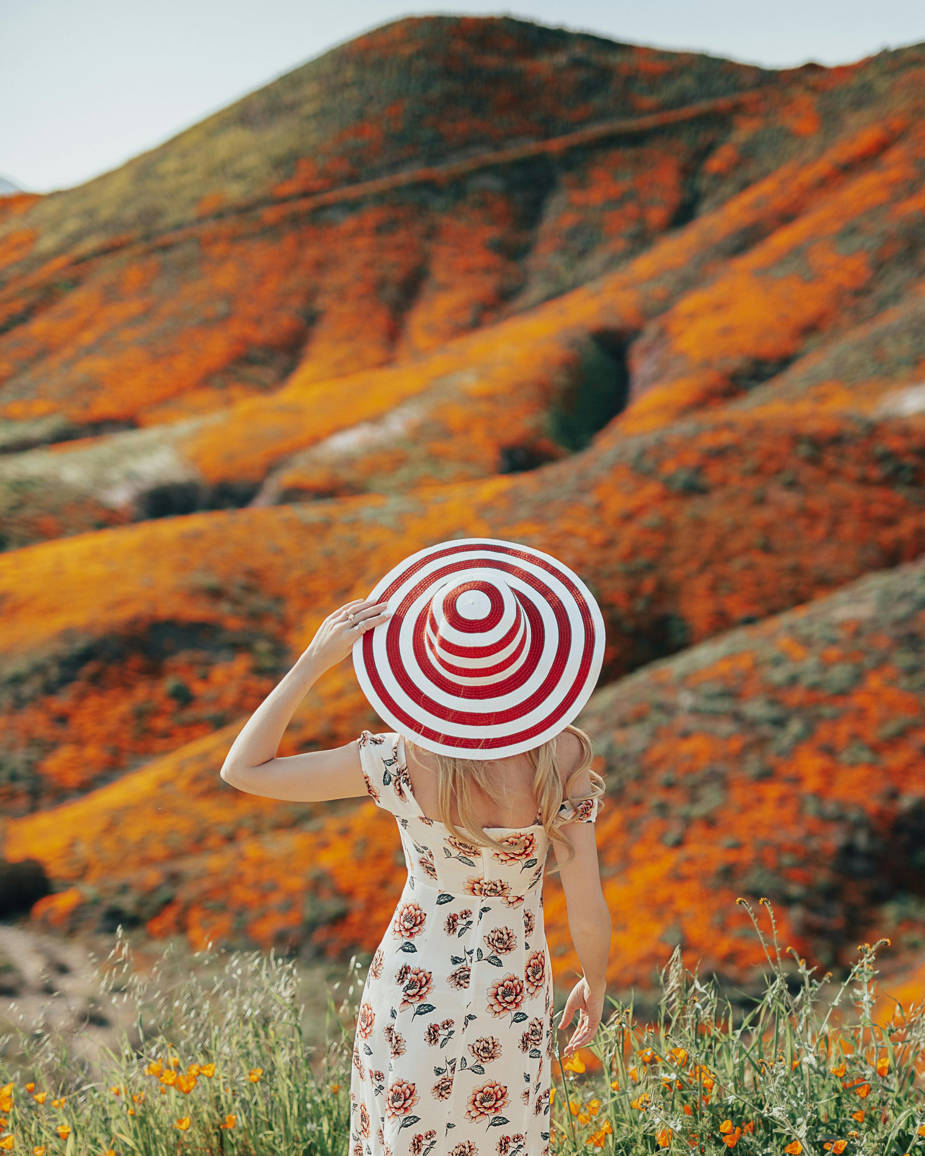 A woman in a floral dress and sun hat observes a super bloom of orange flowers in Lake Elsinore, CA.