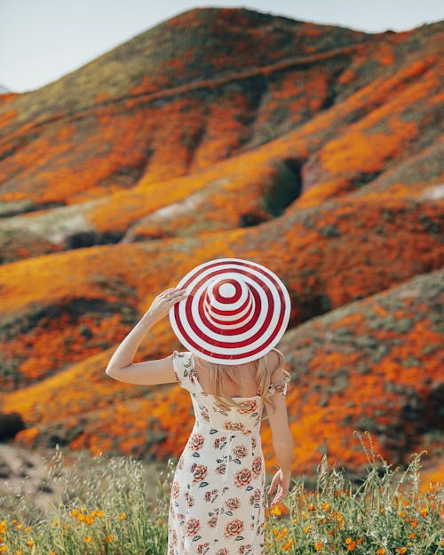 Free Shallow Focus Photo of a Woman in Floral Dress and Sun Hat Standing near Orange Flowers Stock Photo