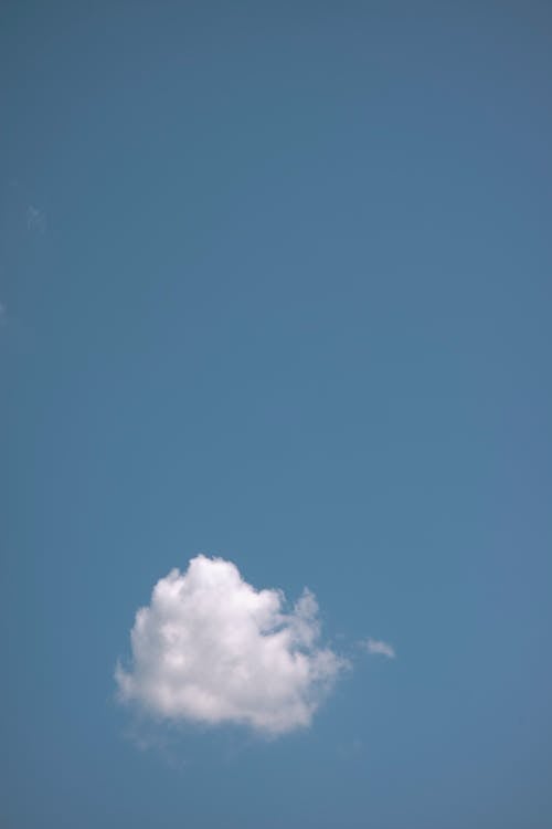 Single white fluffy cumulus cloud floating high in air on clear blue sky on summer day in nature with sunlight