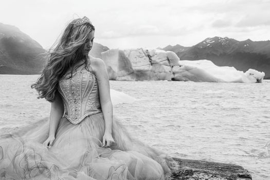 Black and white portrait of a woman in a gown by icy shore, with mountains.