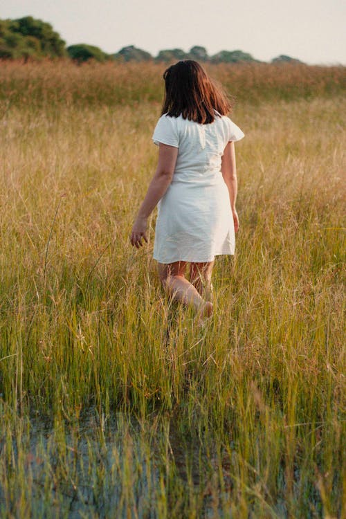 Free A Woman in White Dress Standing on the Grassy Field Stock Photo