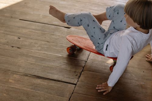 Free A child skillfully balancing on a red skateboard indoors on a wooden floor. Stock Photo