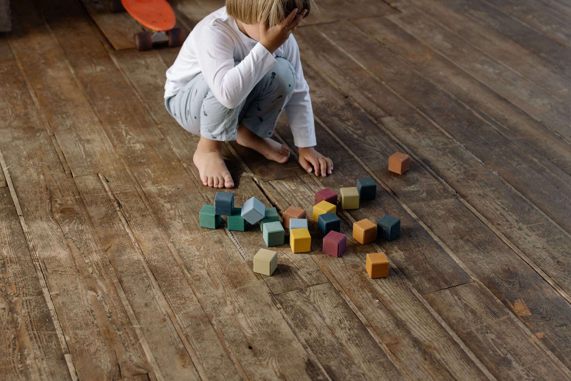 A child engages with colorful wooden blocks on a wooden floor, indoor play setting.