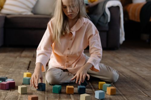 Free A young girl sits indoors playing with colorful wooden cubes on the floor. Stock Photo