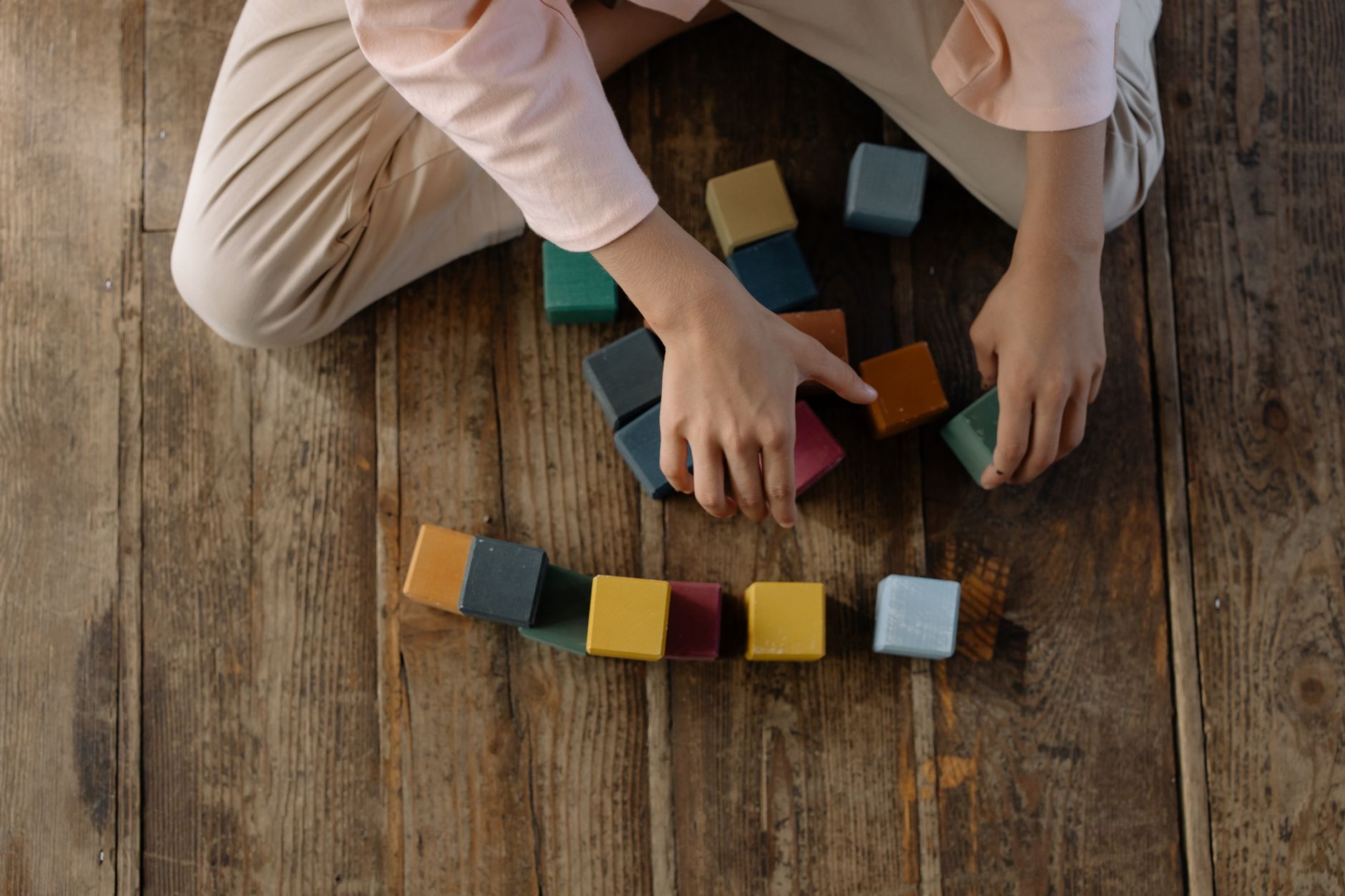 Child arranging colorful toy blocks on a wooden floor, creativity at play.