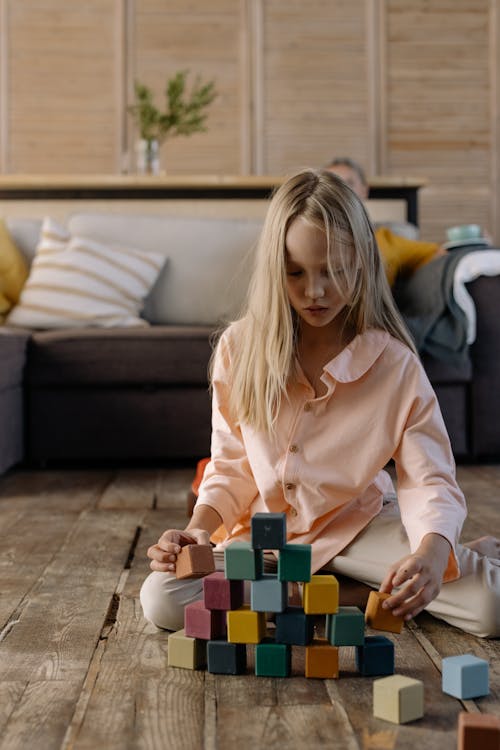 A Girl Stacking Colorful Blocks while Sitting on a Wooden Flooring