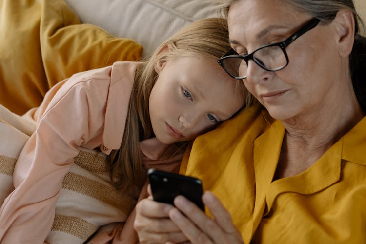 Close Up Photo Of Elderly Woman And A Girl Looking At The Screen Of A Cellphone