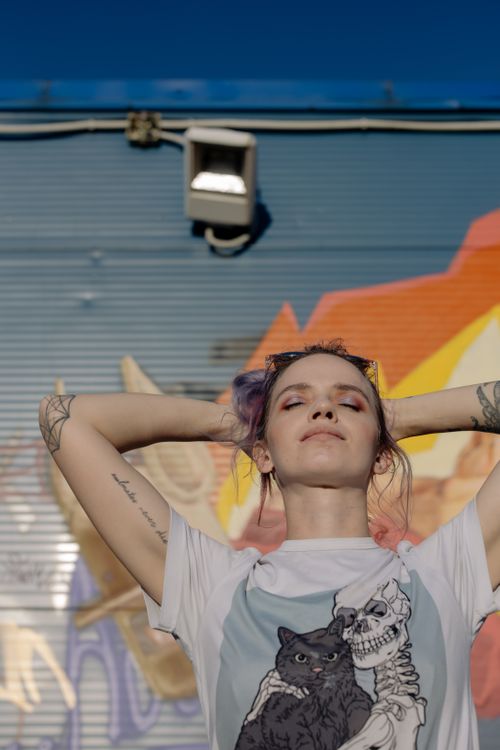 Free A confident woman enjoys the sun against a vibrant graffiti backdrop. Stock Photo