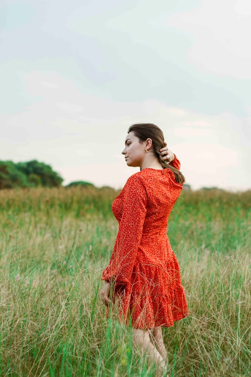 Free Woman in Red Long Sleeve Dress Standing on Green Grass Field Stock Photo