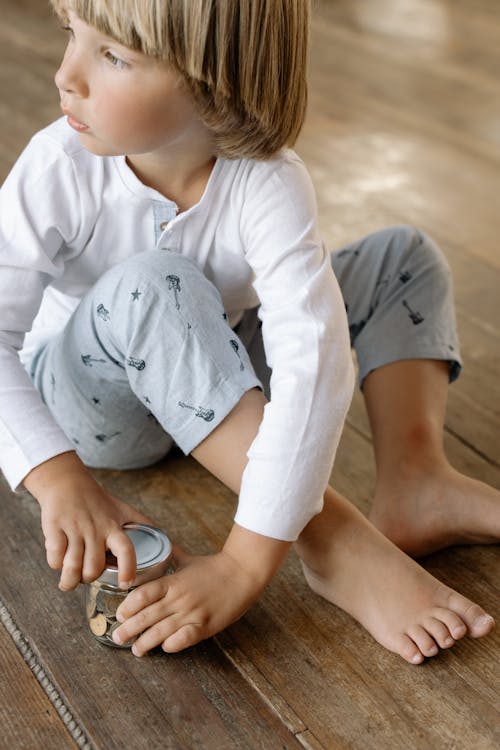 Boy in White Long Sleeve Shirt and Gray Pants Sitting on Brown Floor
