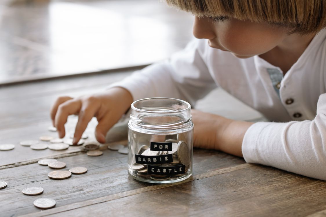 Free A young child collects coins in a jar labeled 'For Barbie Castle', symbolizing saving and dreams. Stock Photo