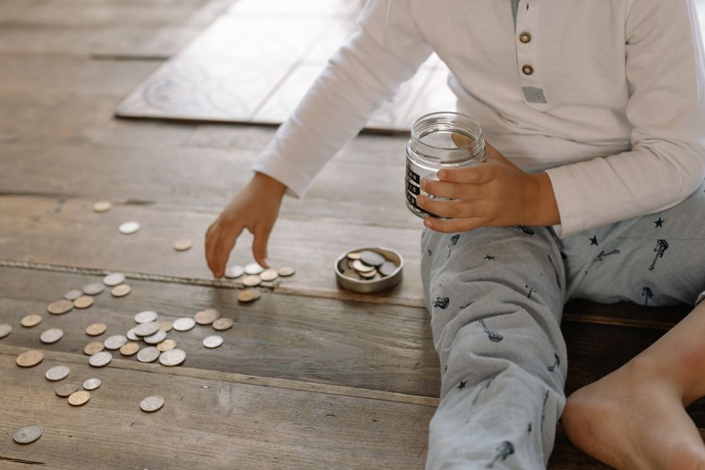 Criança guardando moedas em um pote de vidro