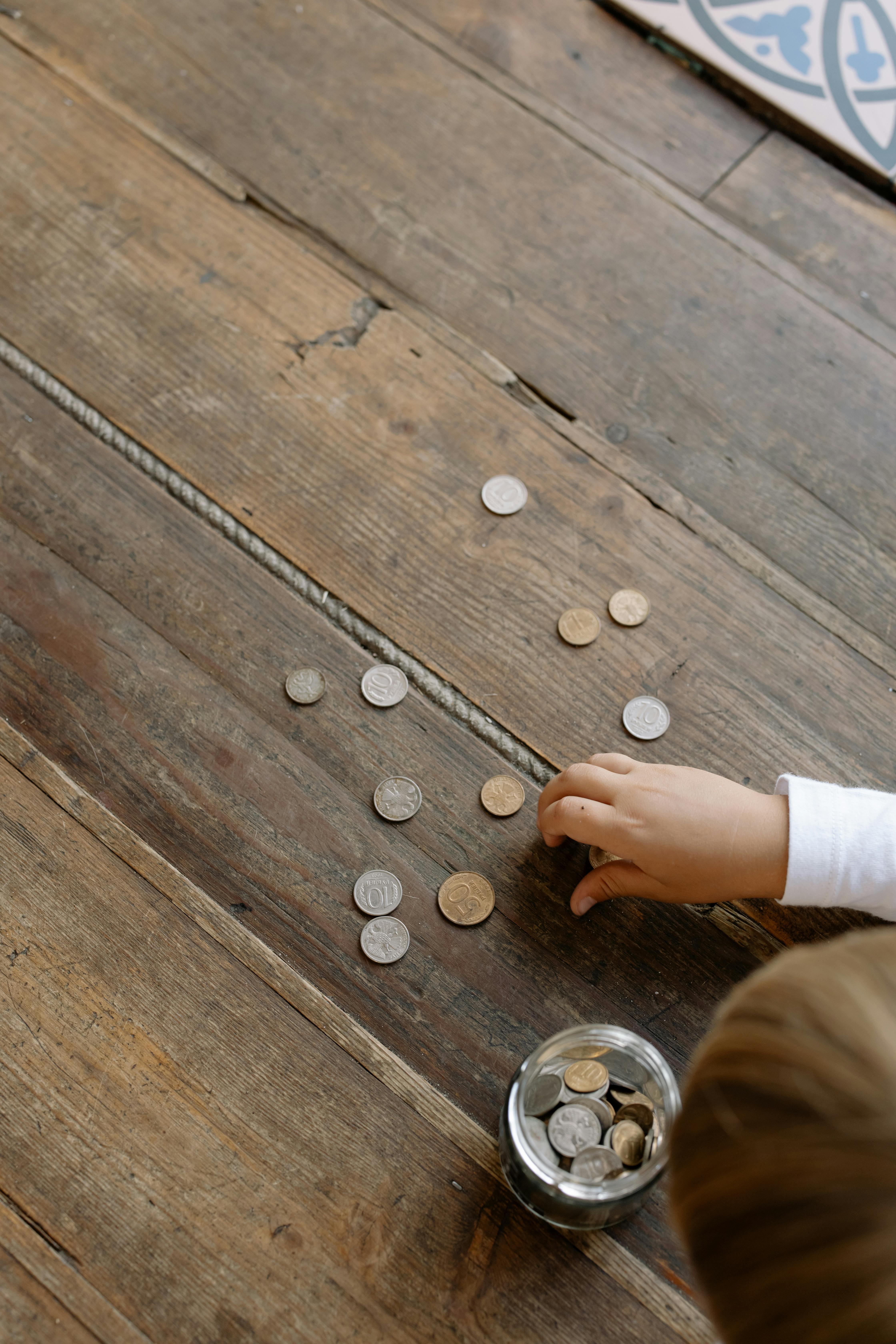 a person picking the coins on the wooden flooring