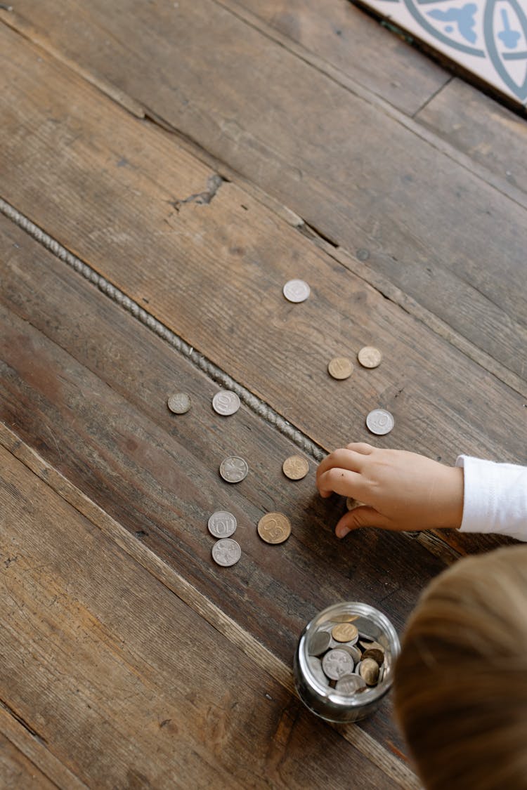 A Person Picking The Coins On The Wooden Flooring