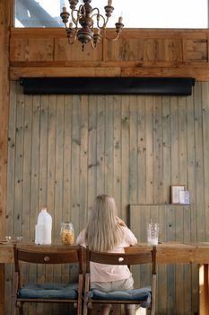A young girl sitting at a rustic wooden table having breakfast in a cozy setting.