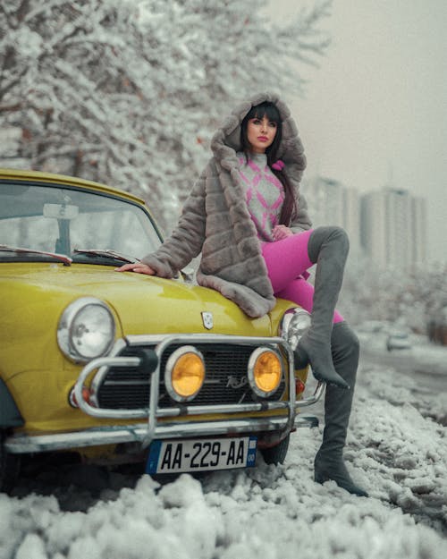 Free Woman in Gray Fur Coat Sitting on Yellow Car Stock Photo