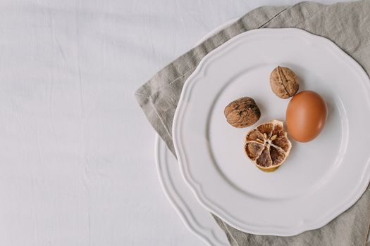Artistic still life featuring a dried lemon, walnuts, and an egg on a white plate.