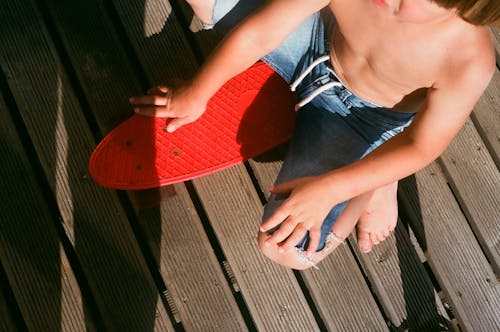 Overhead Shot of a Boy in Denim Shorts Sitting on a Red Penny Board