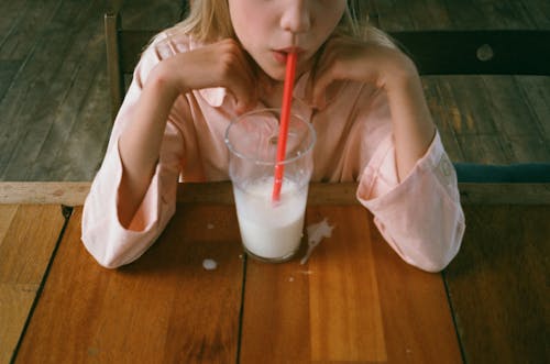 Photo of a Girl in a Pink Shirt Sipping Milk from a Red Straw