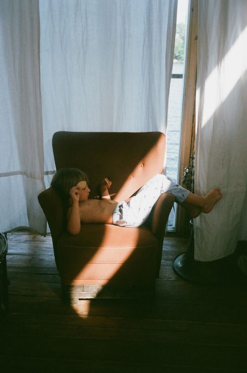 Free A young boy relaxing on an armchair by a window, enjoying a sunny day indoors. Stock Photo