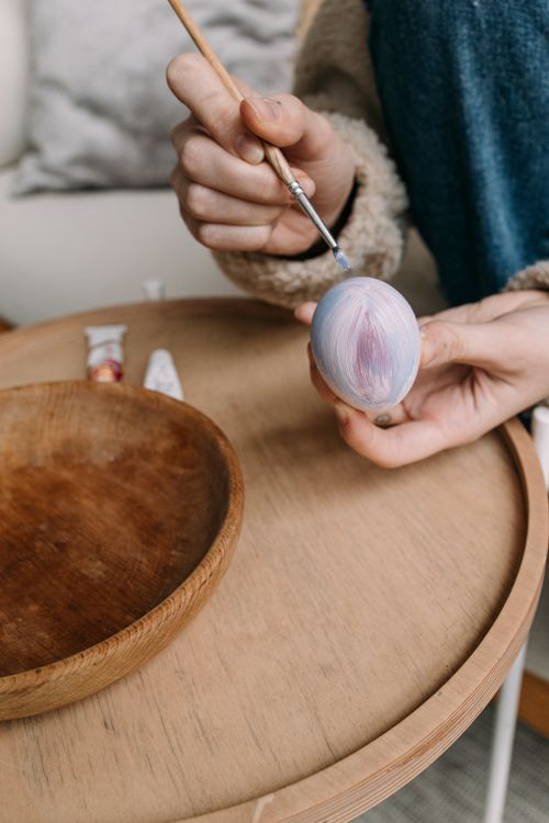 Free Hands painting an Easter egg with a brush in a cozy indoor setting. Stock Photo