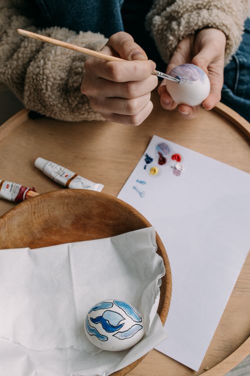 Free Hands painting Easter eggs with vibrant colors indoors. Creative holiday activity. Stock Photo