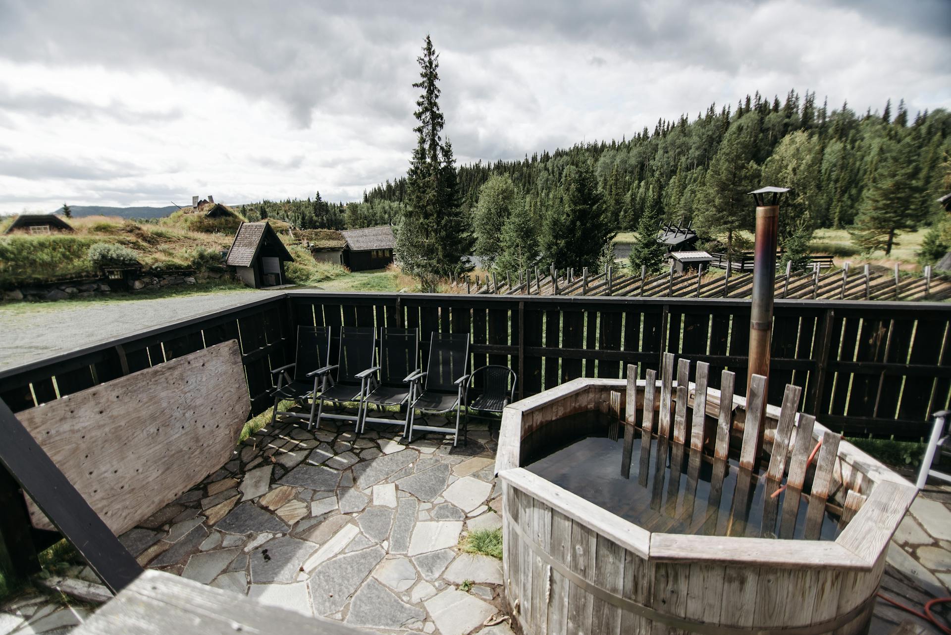 Serene rural scene featuring a wooden hot tub on a patio with forest views.