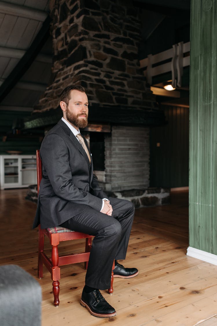 Man In A Black Suit Sitting On A Brown Wooden Chair