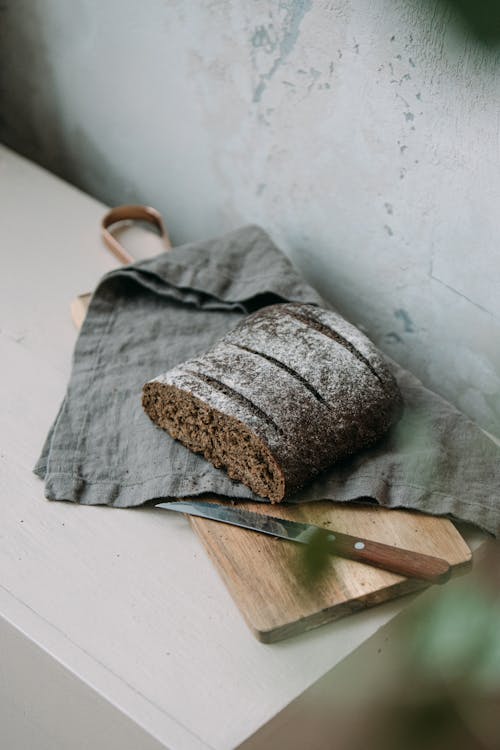 Half of a Black Loaf of Bread on a Wooden Chopping Board