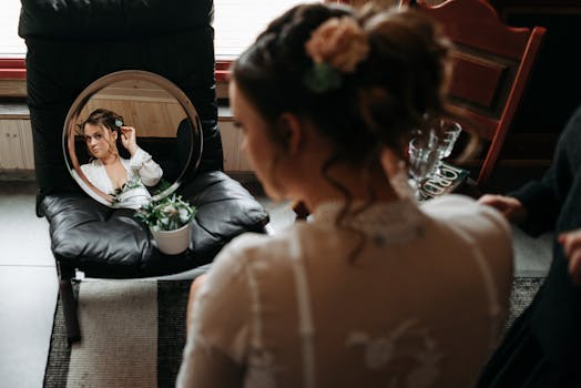 A bride adjusts her hair while looking into a round mirror indoors.