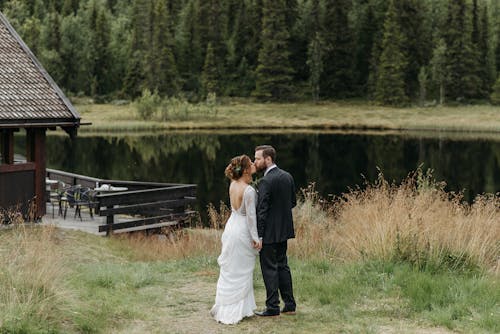 A Newlywed Couple Standing on a Grass Field Near the Lake