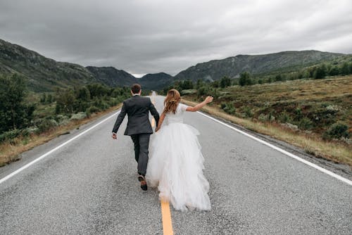 Back View of a Groom and a Bride Running in the Middle of a Road