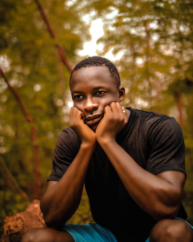 Man Crouching With His Face In His Hands In A Forest 