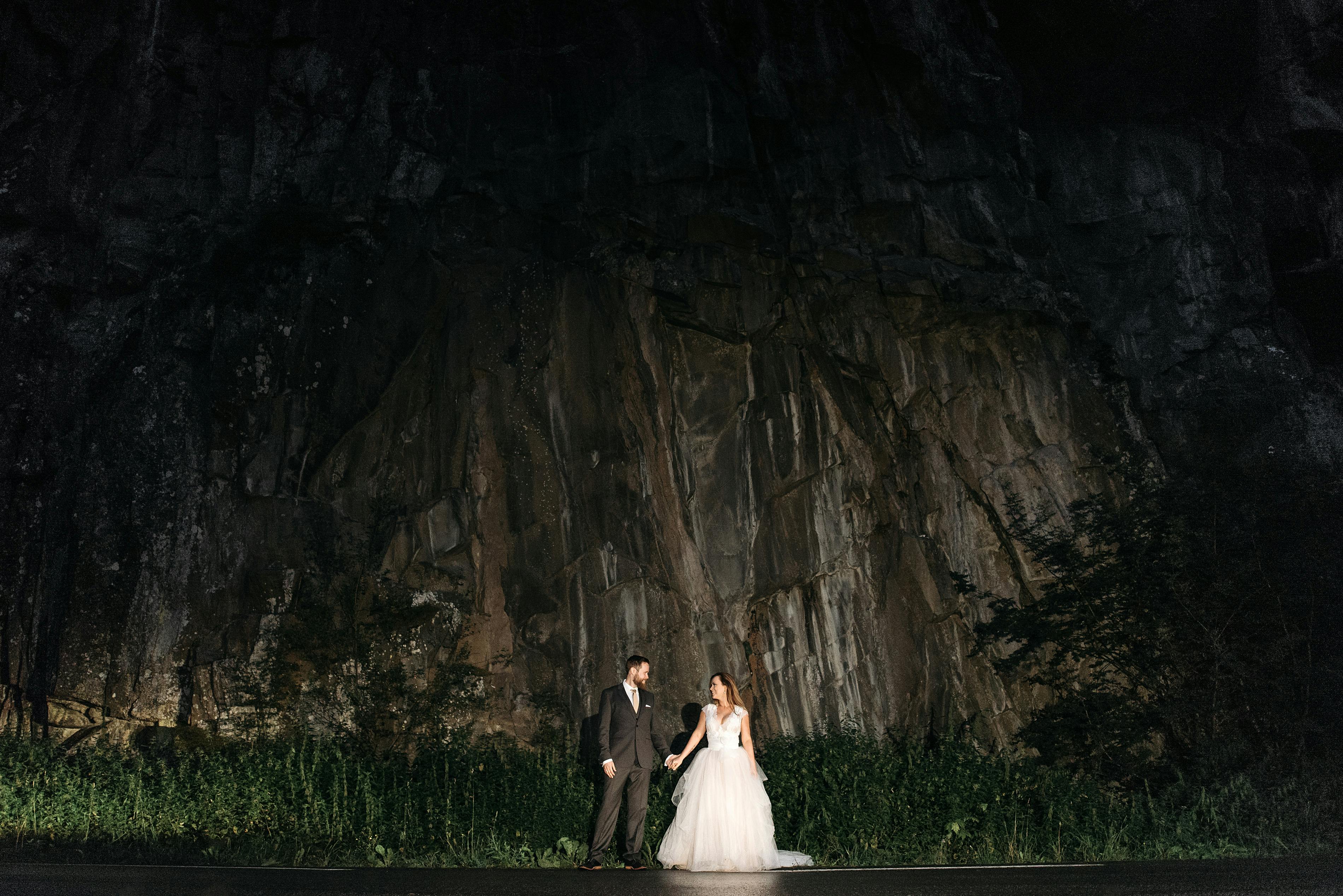 Bride and groom pose romantically against a rocky backdrop, adding a mystical touch to their wedding.