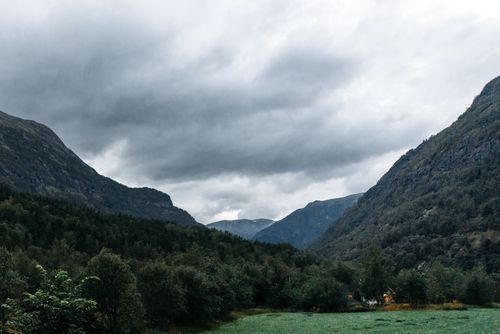 Free Explore a breathtaking mountain valley with dense forests beneath a dramatic and moody sky. Stock Photo