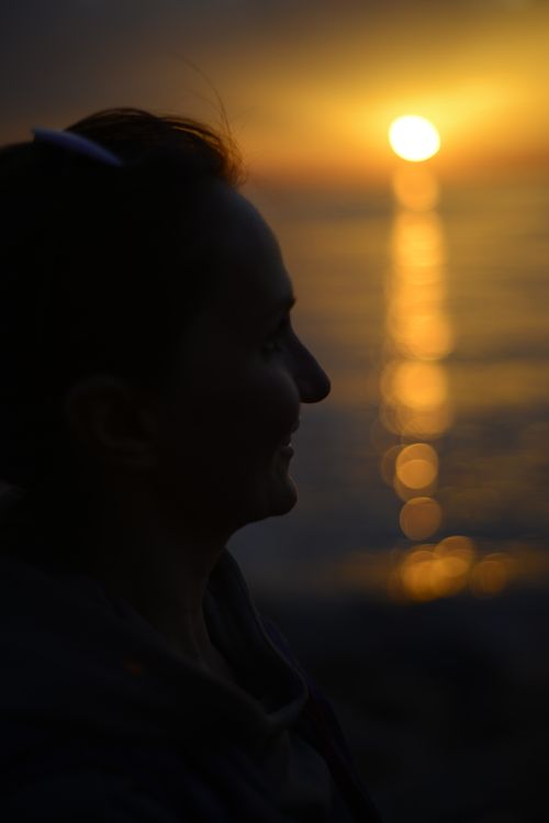 Free A woman smiles in silhouette against a vibrant sunset over the ocean, capturing tranquility. Stock Photo